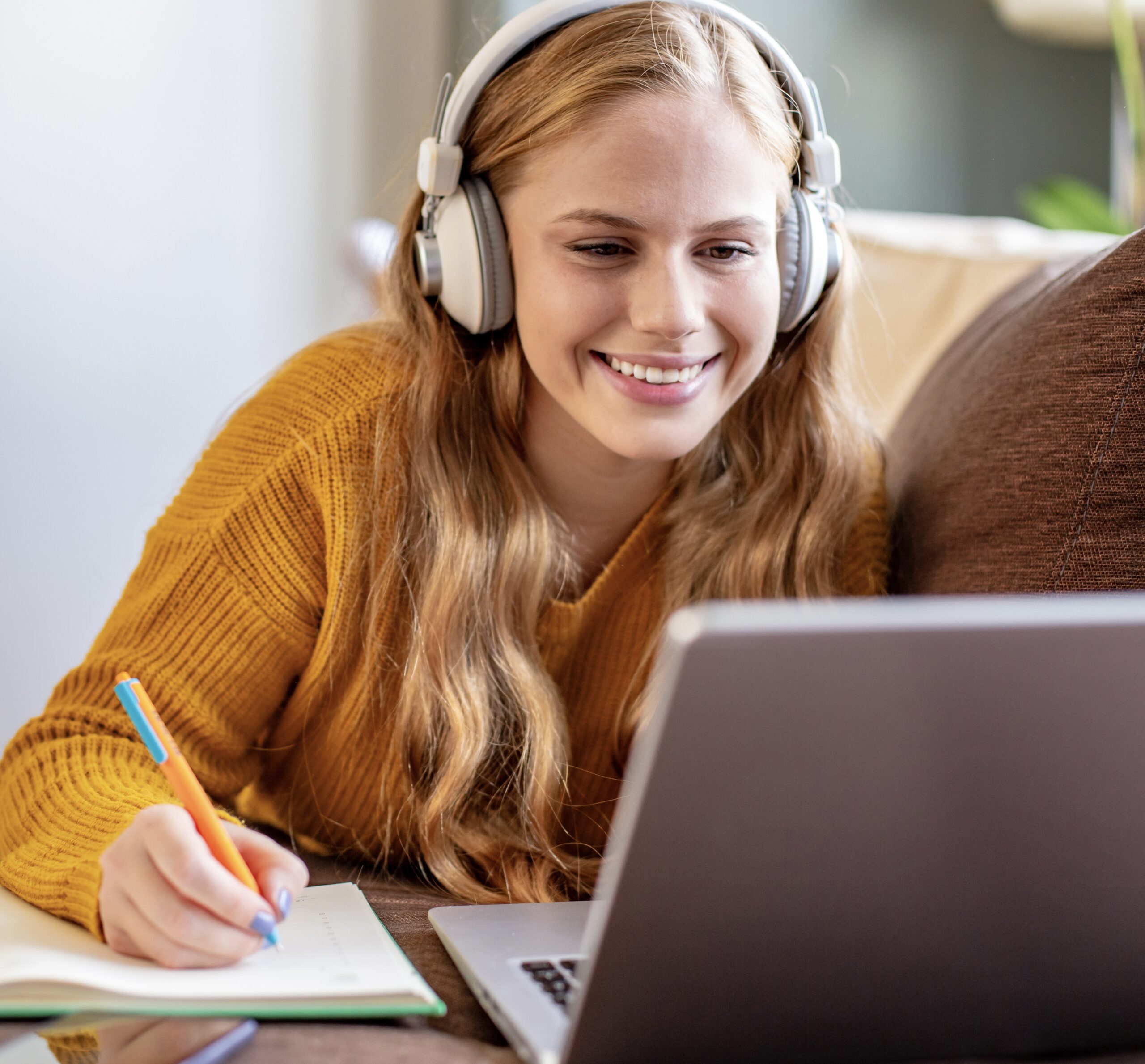 Photo of young woman writing notes while listening to online class